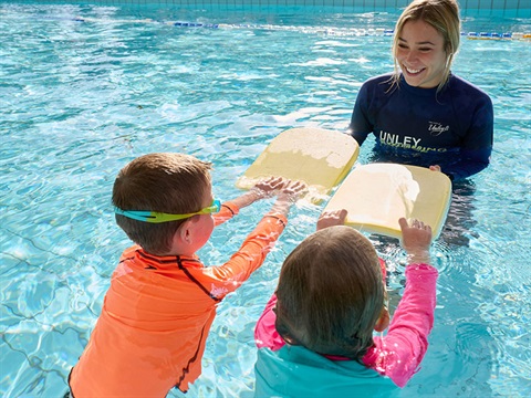 instructor helping children use paddle boards in pool