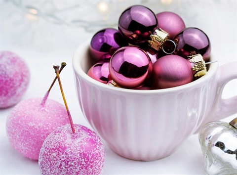 Pink and purple shiny baubles in a cup beside sugared cherries