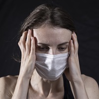 Masked woman looking anxious with her hands at the side of her head.