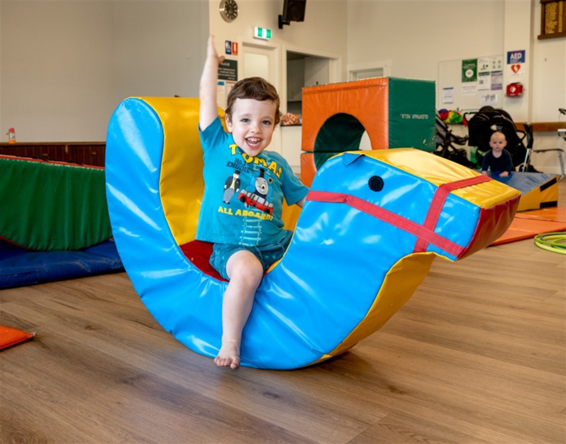 A young boy playing on a large rocking horse toy made out of cushion mat