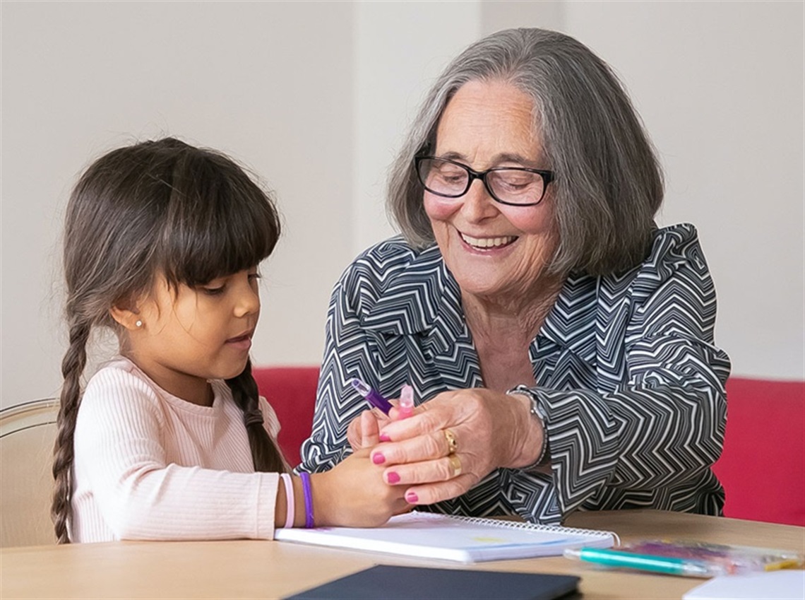 An older woman playing with a young girl drawing on a table