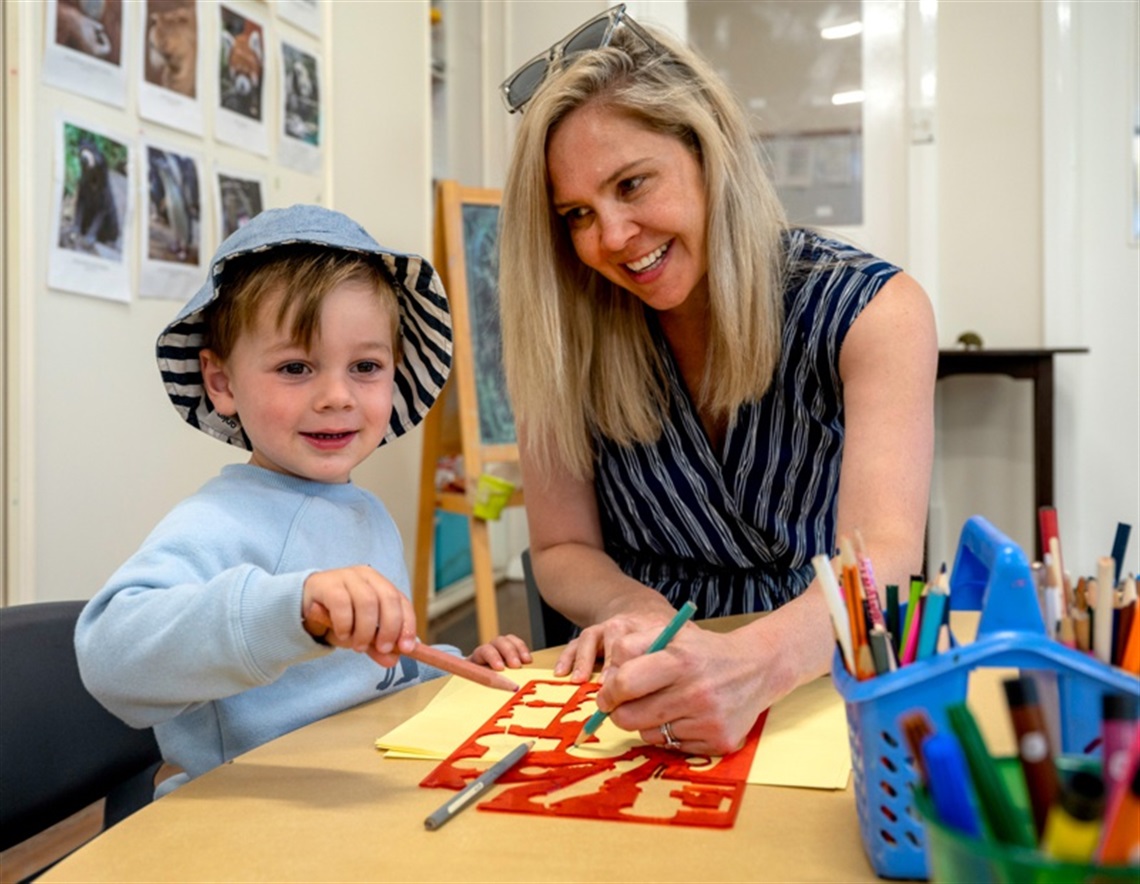 A mother playing with her child - drawing on a table with pencils and a stencil