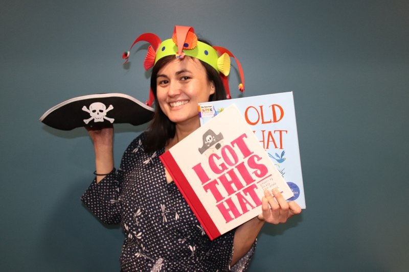 Library staff member holding books, pirate hat and wearing an example of the jester hat craft