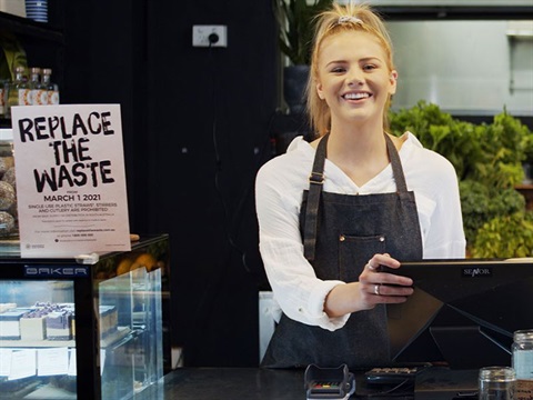 Young woman standing at service counter of cafe ready to take order